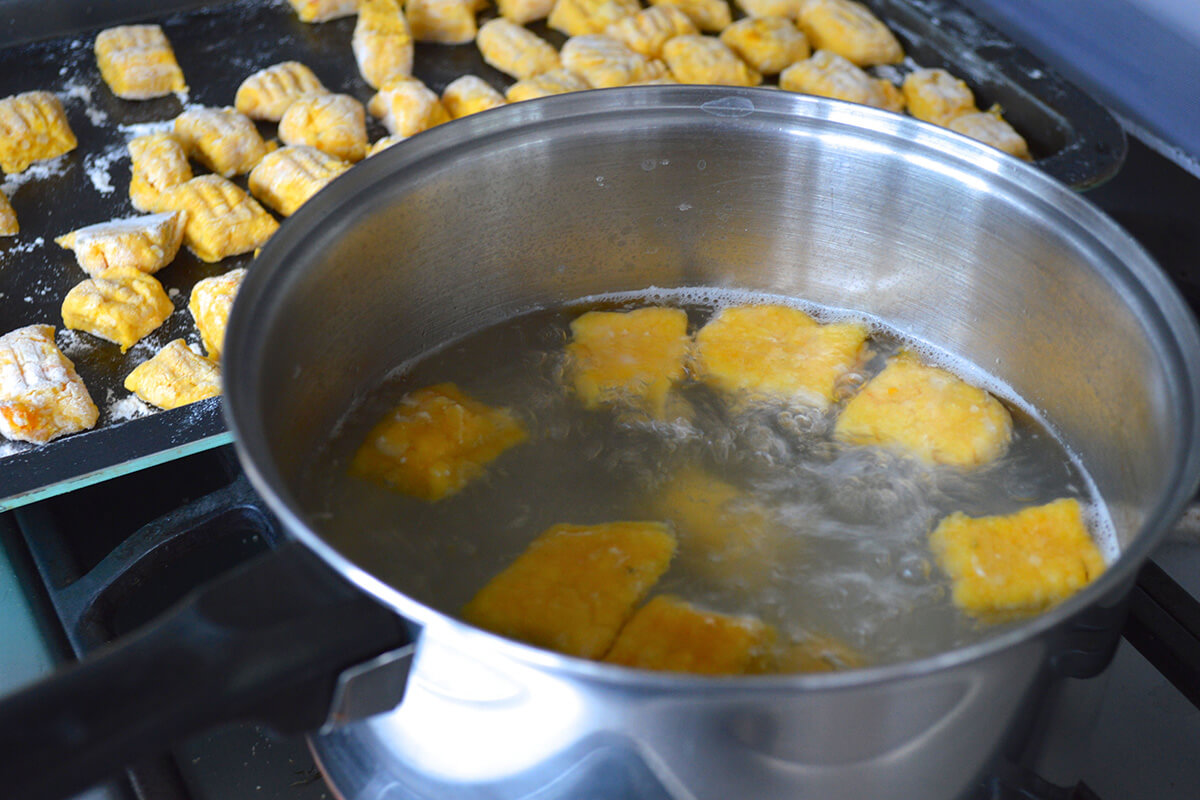 A saucepan of gnocchi being cooked, next to a baking tray with gnocchi balls