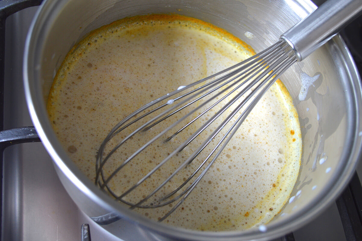 A saucepan of Golden Spiced Milk ingredients being whisked together