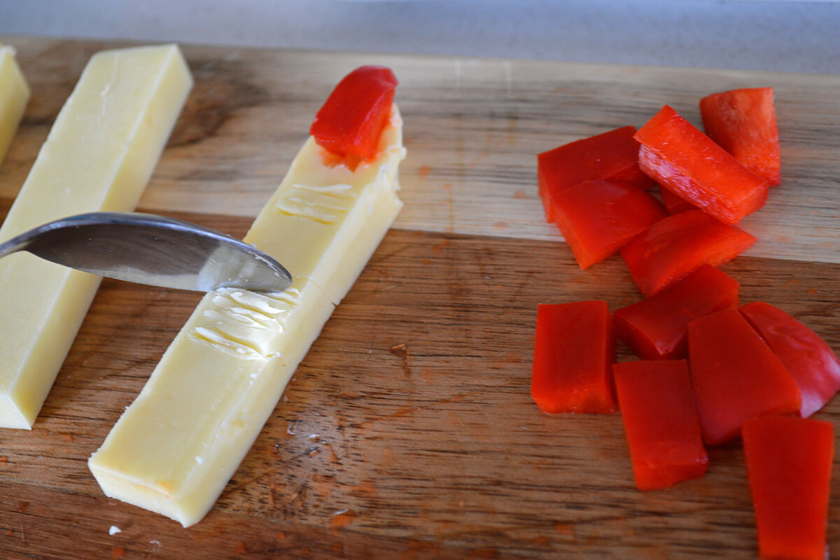 A chopping board with cheese sticks and red pepper