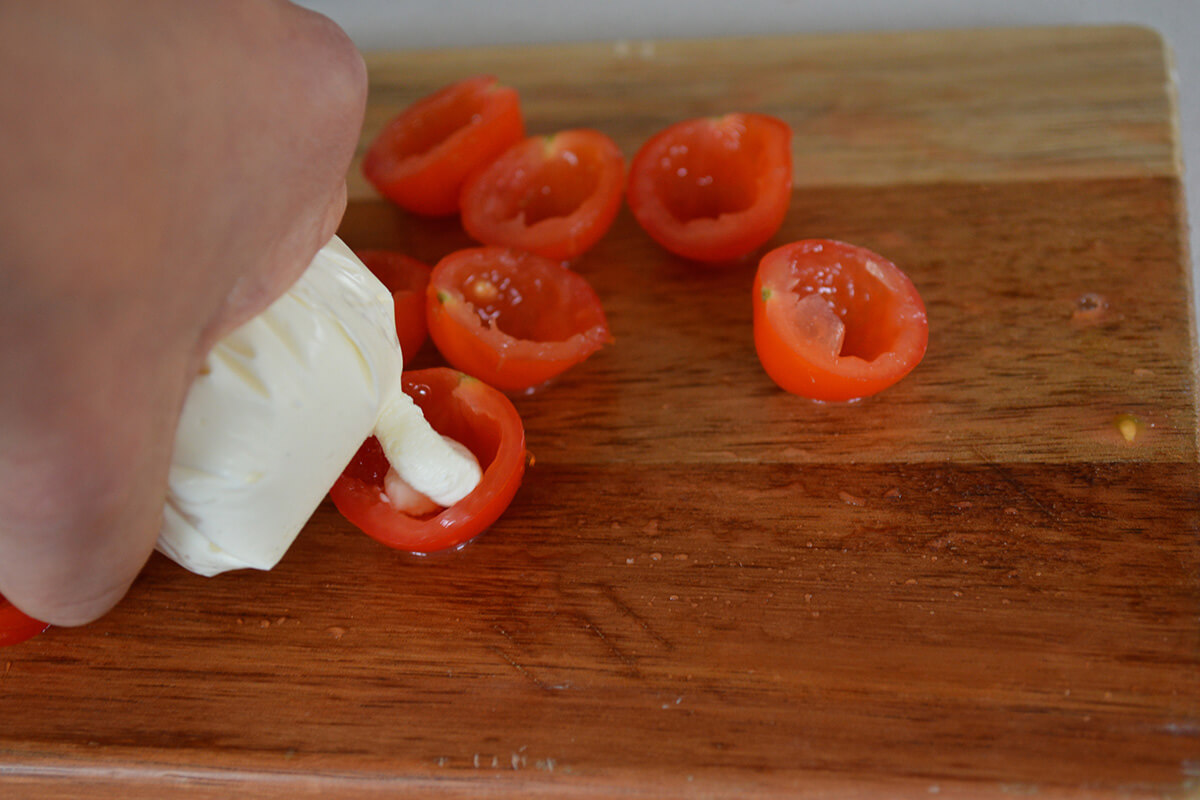 A chopping board with cherry tomatoes being stuffed with cream cheese