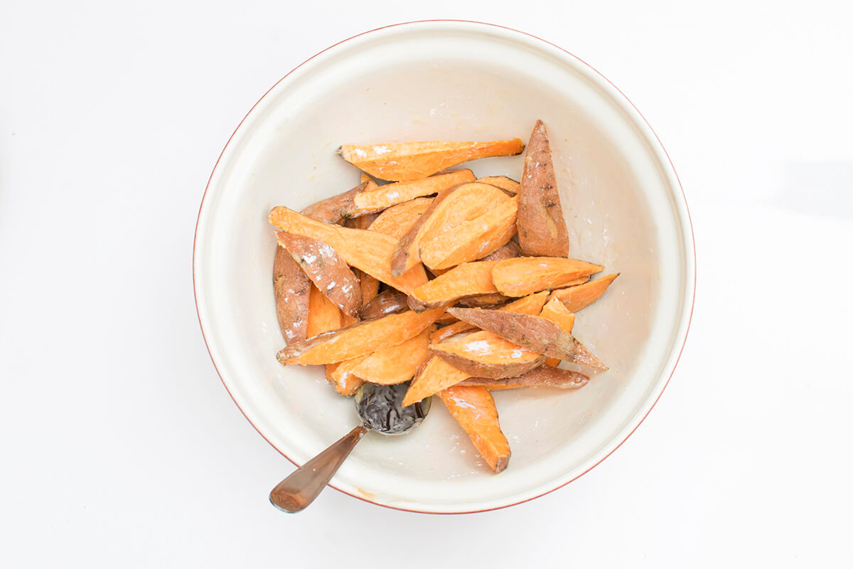 A bowl with chopped sweet potato wedges with oil and cornstarch