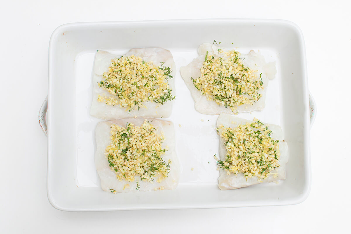 A baking dish with fish topped with herby almond mix