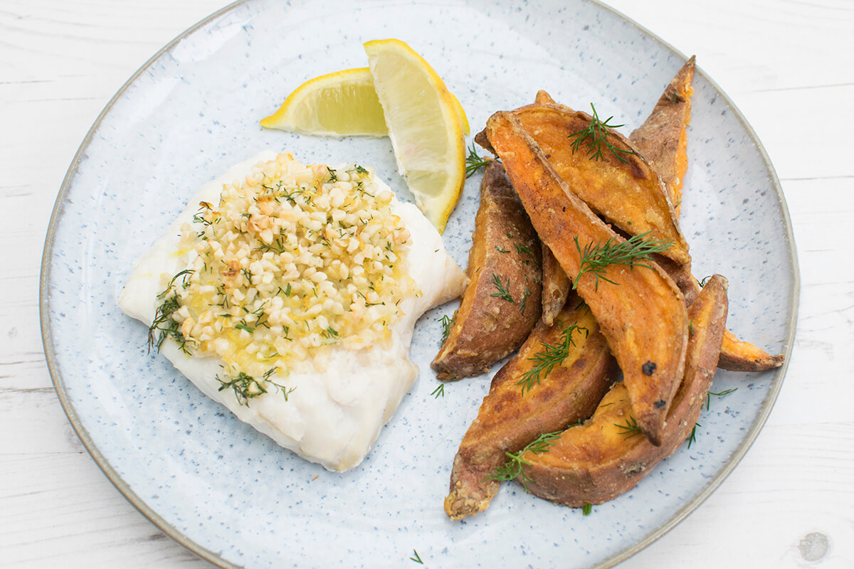 A plate of fish served with sweet potato fries and lemon wedges