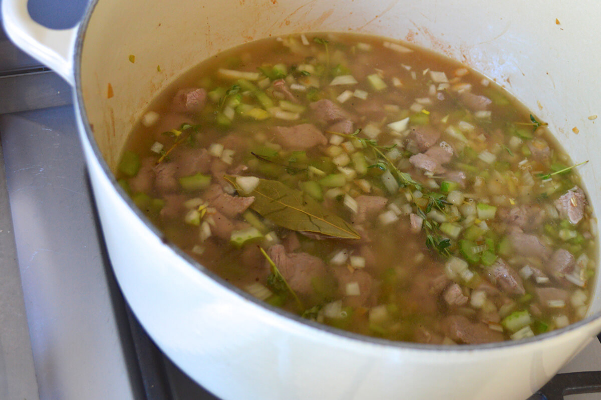 Lamb in a saucepan with onion, celery, herbs and stock