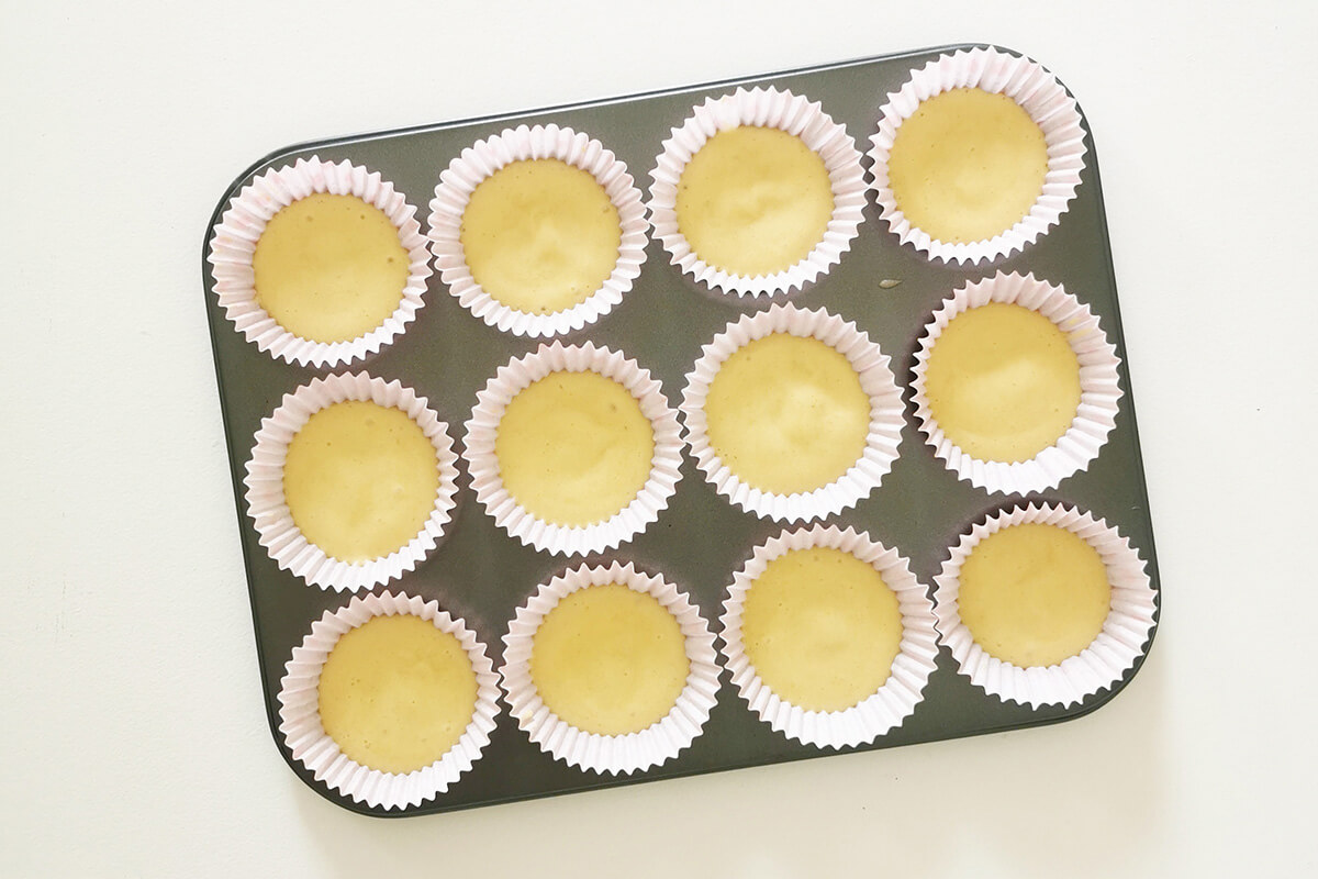 A 12 space cupcake tin with paper cake cases filled with cupcake batter