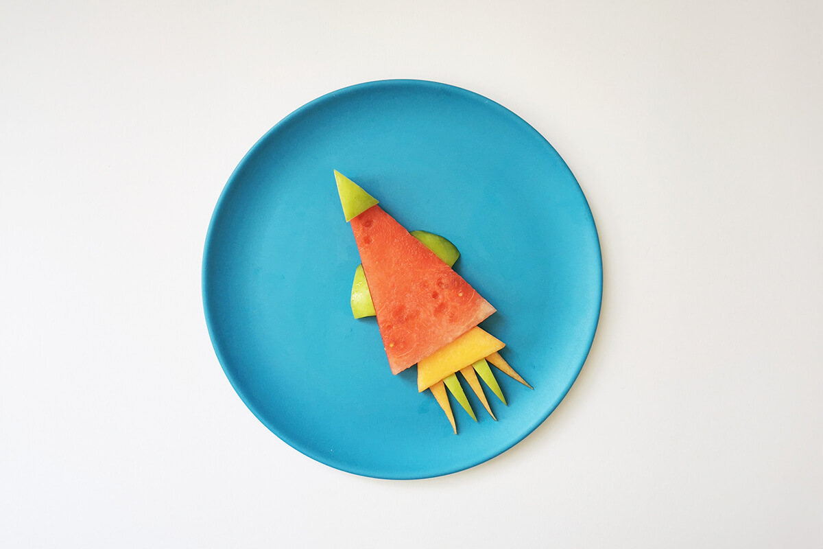 Mini finger cantaloupe slices and apple slices arranged alternating at the bottom of the rocket shape to create flames