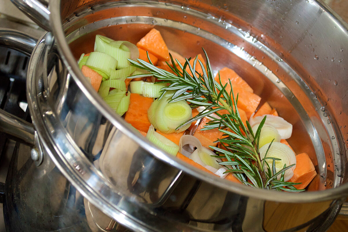 Peeled, diced sweet potato and sliced leek in a steamer with a sprig of rosemary