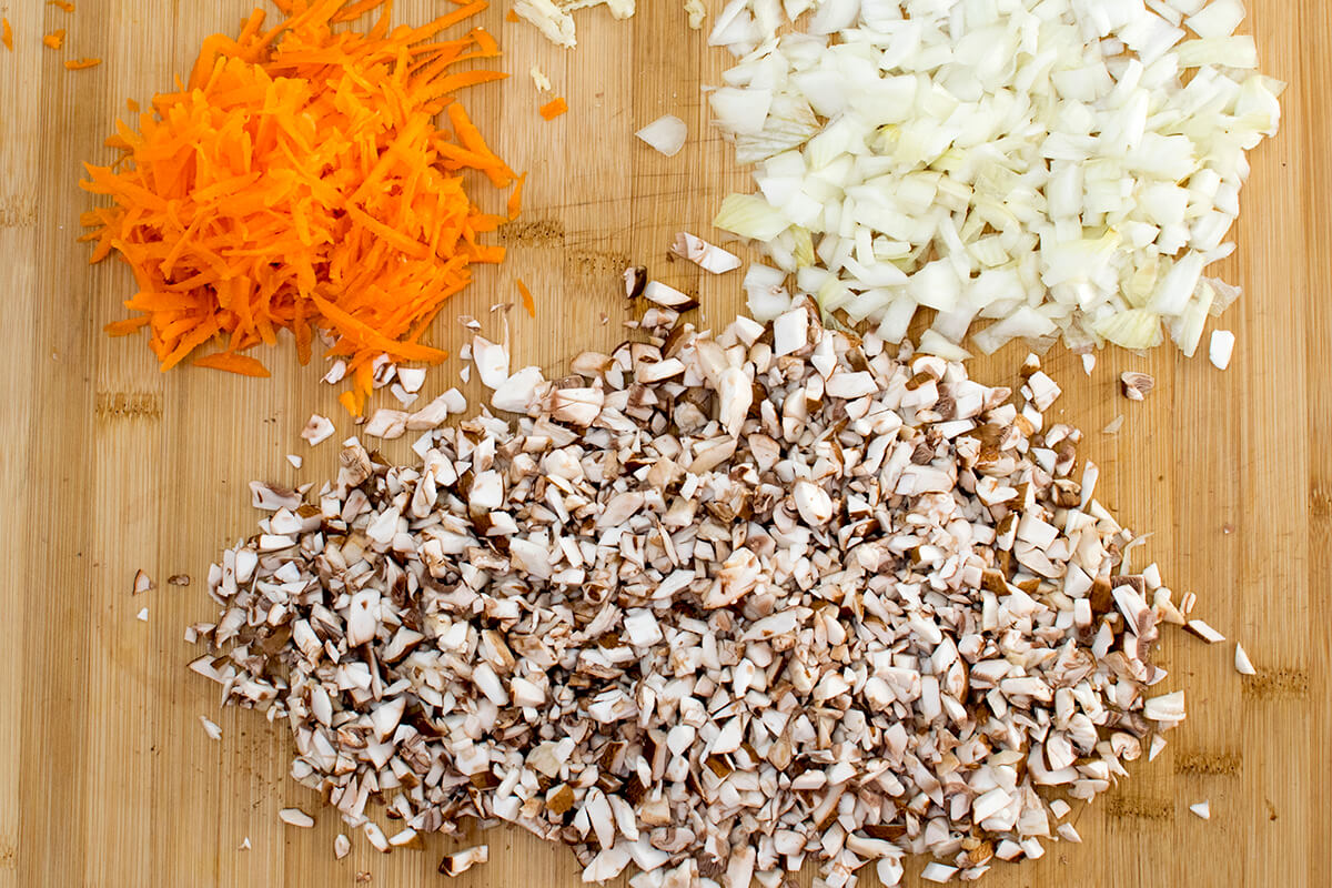 A chopping board with grated carrot, finely chopped onion and mushrooms