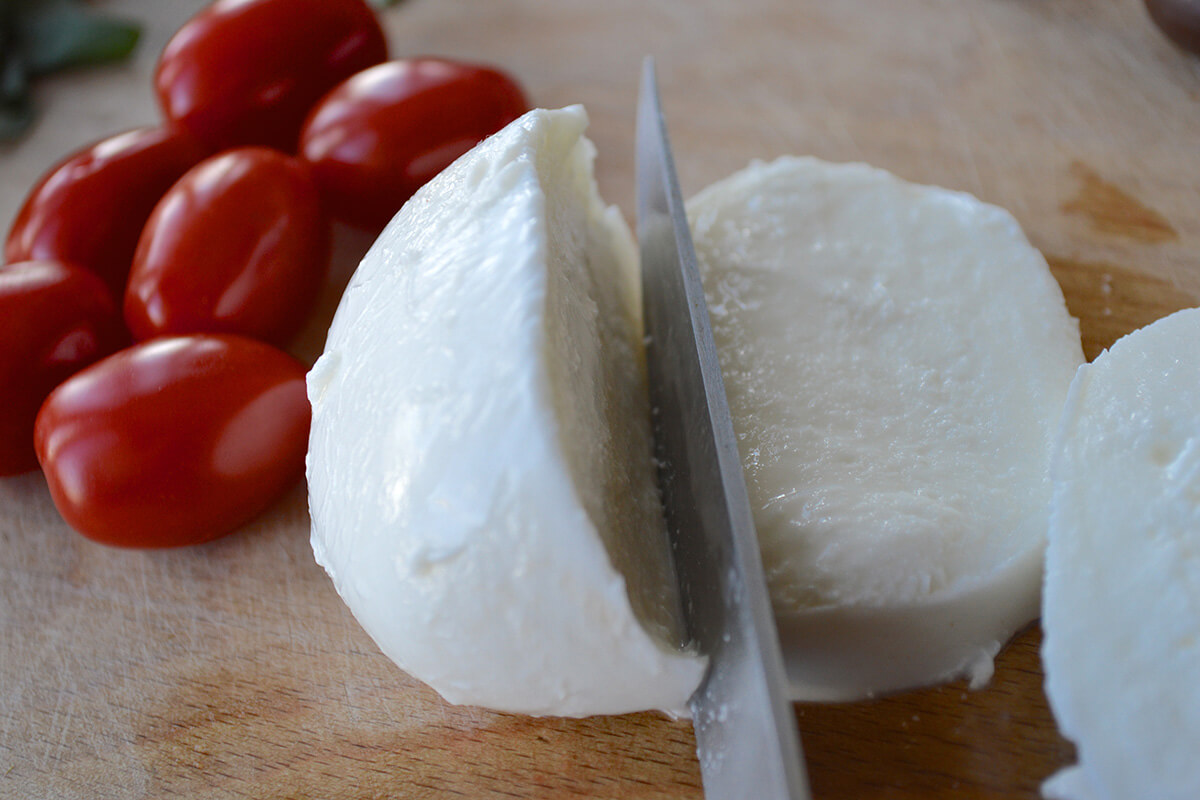 A chopping board with cherry tomatoes and a ball of mozzarella being sliced