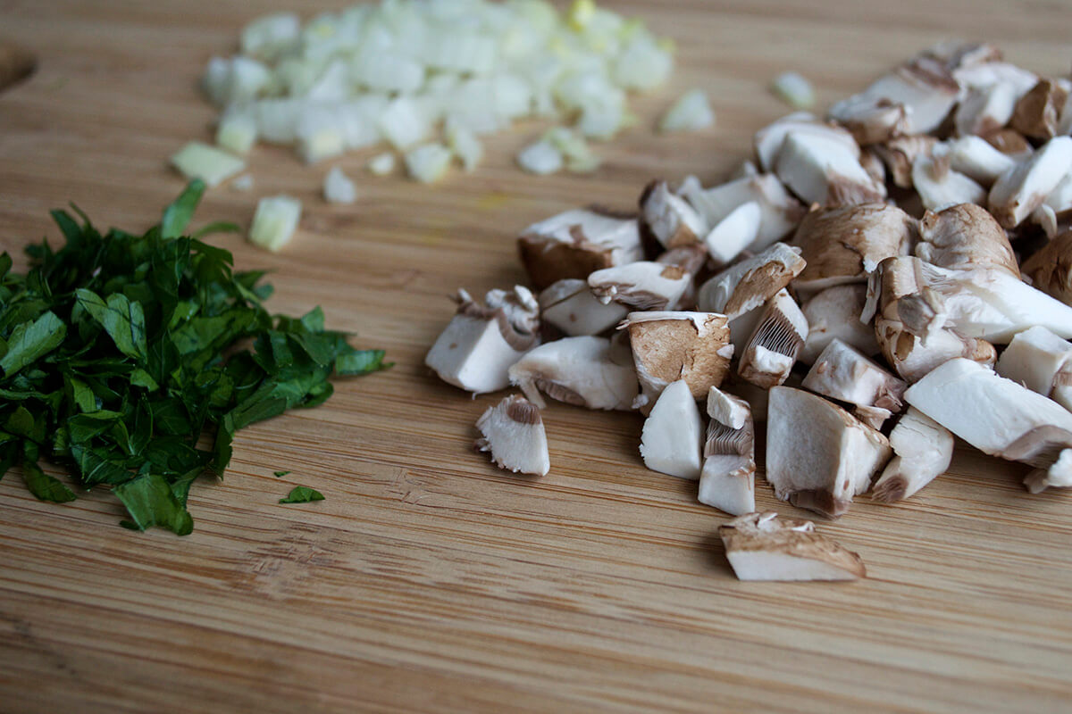 A chopping board with chopped onion, mushroom and fresh herbs