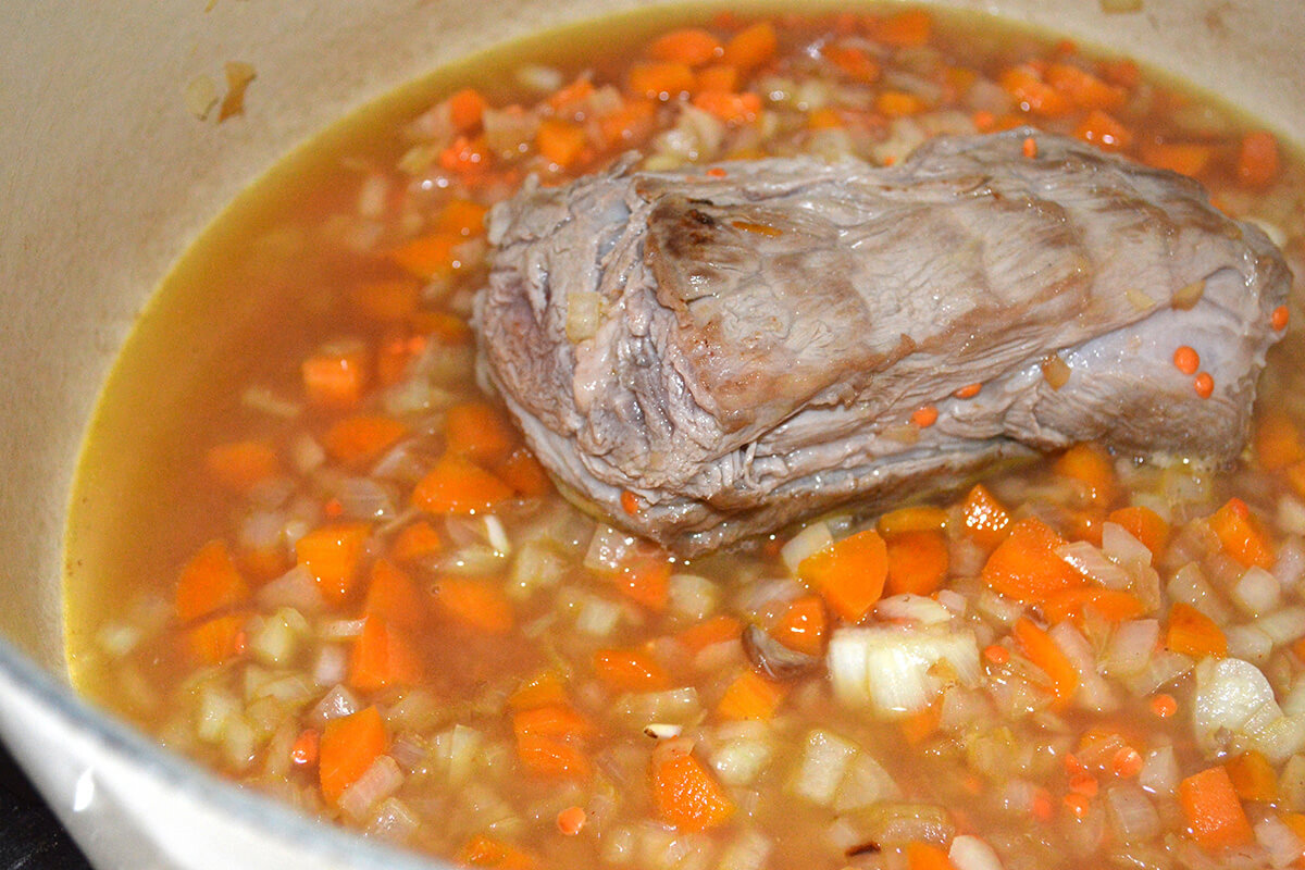 Lamb fillet in a saucepan with onion, carrot, lentils and water