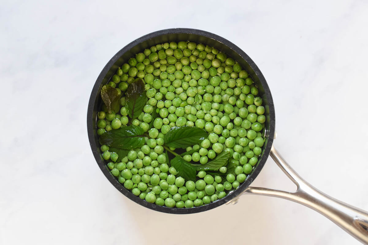 Peas and mint leaves in a saucepan of water