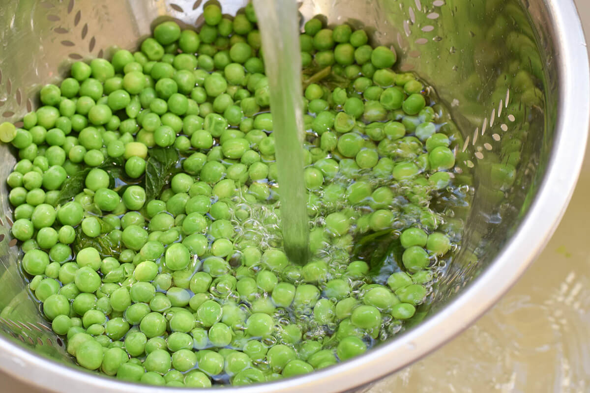 Peas and mint leaves being in a colander being run under a tap