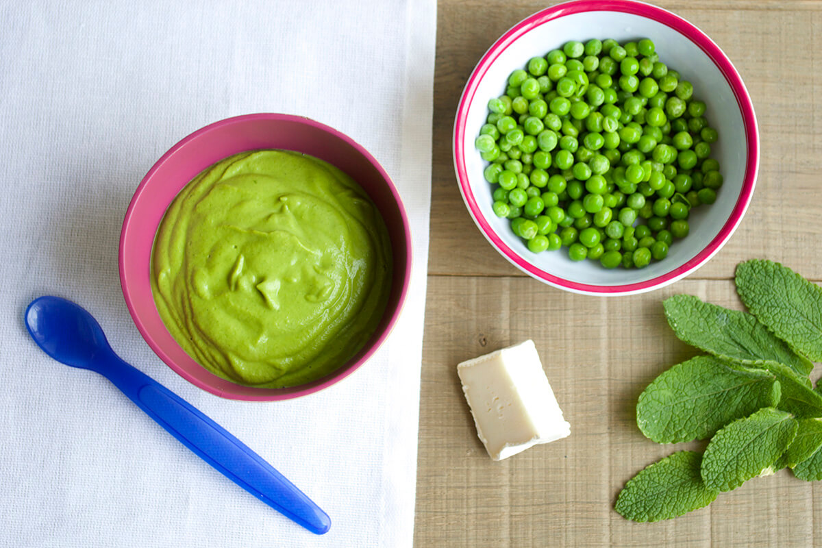 A bowl of Pea & Mint Puree with Goat Cheese next to a bowl of peas, some goats cheese and mint leaves