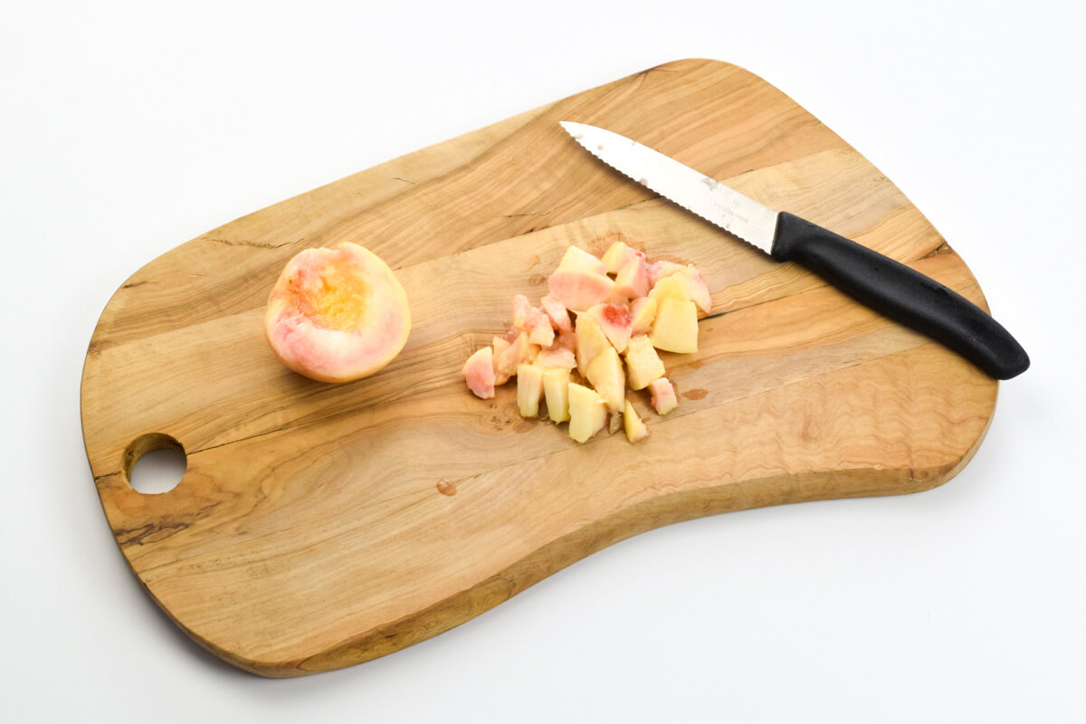 A wooden chopping board with a halved peach and some diced peach