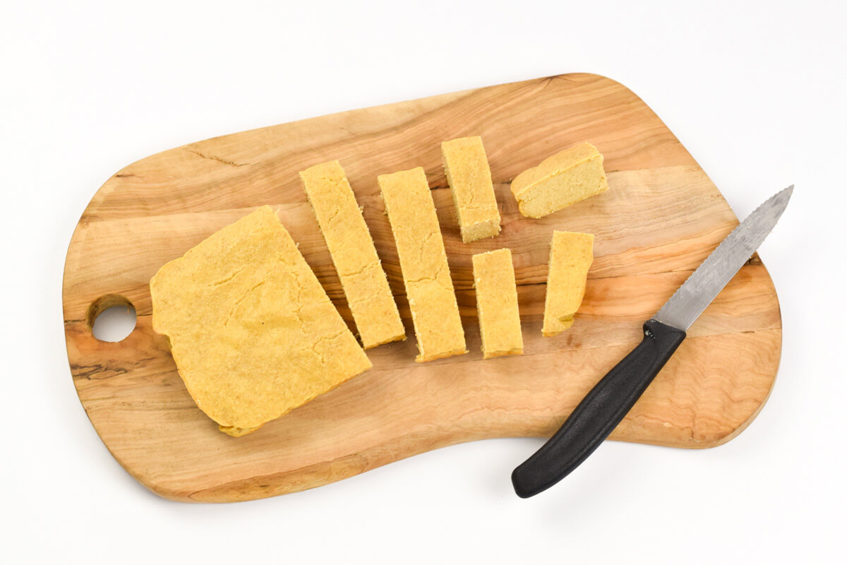 A wooden chopping board with a loaf of peach baked oat fingers, with some cut into slices