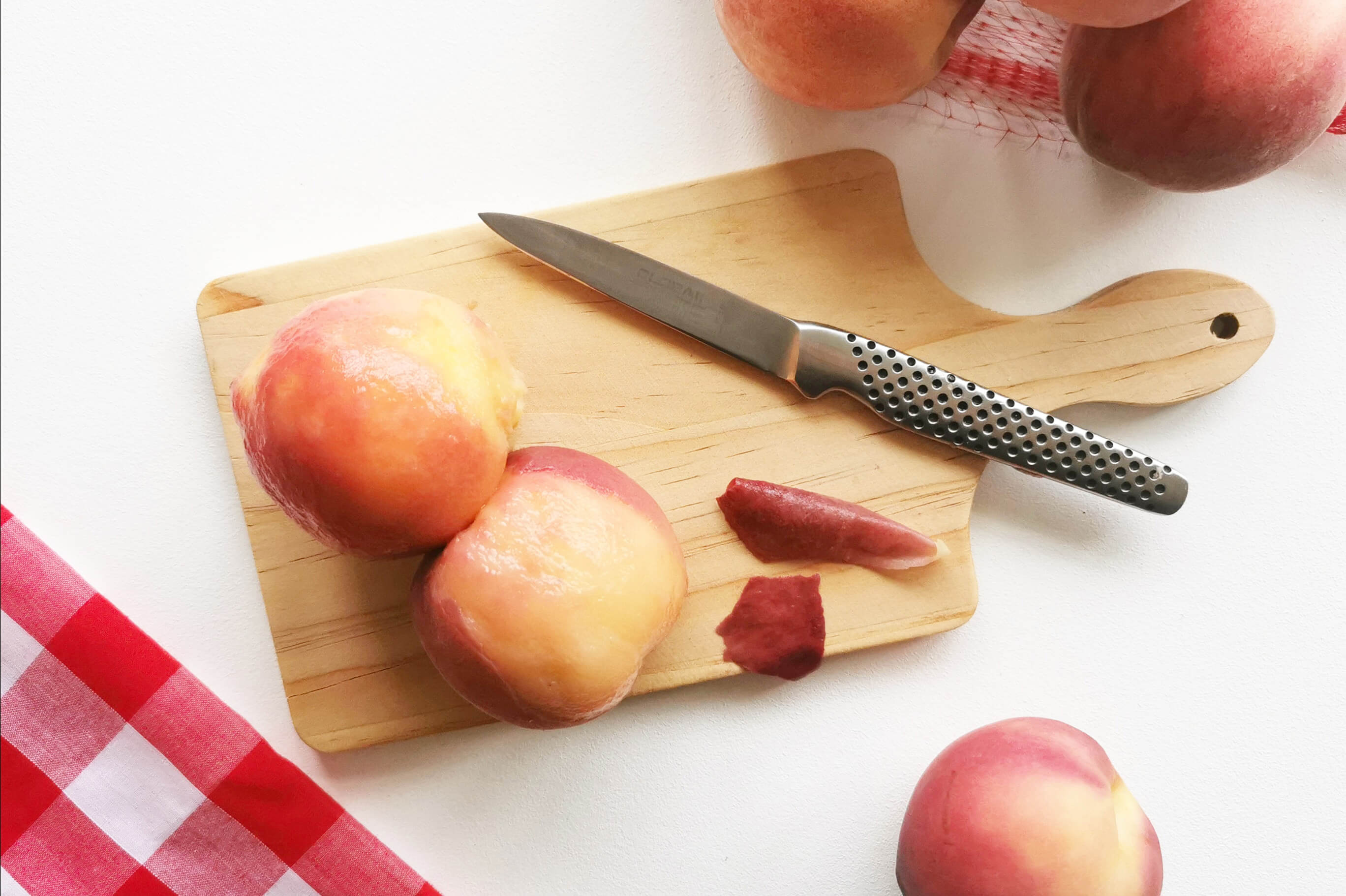 A chopping board with two peaches on it and some removed peach skin