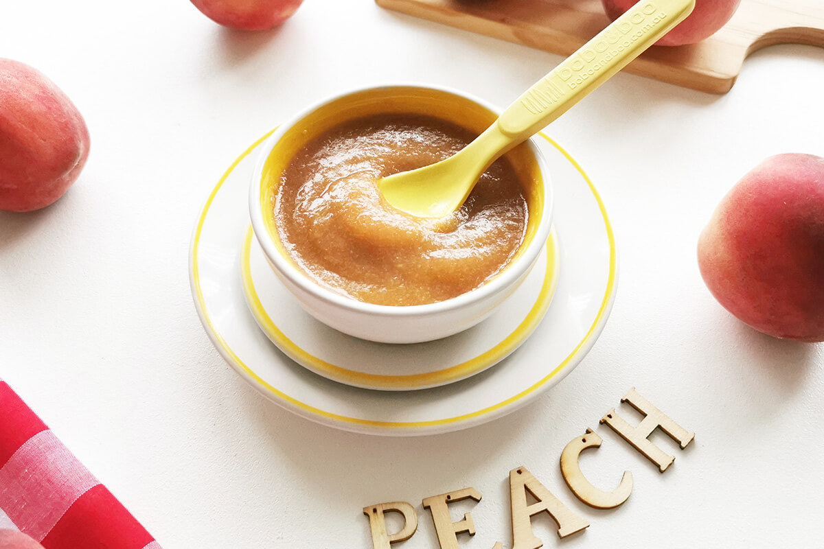 Peach puree in a bowl with some peaches around it