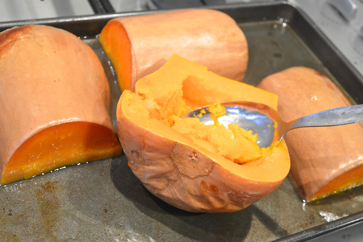 Two halved butternut squash on a roasting tray having the inside scooped out