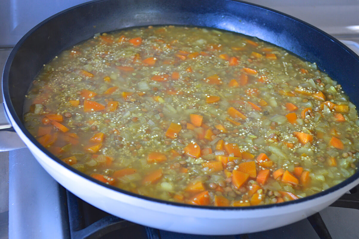 A frying pan of chopped onion, ginger and garlic with carrots, lentils, quinoa and stock