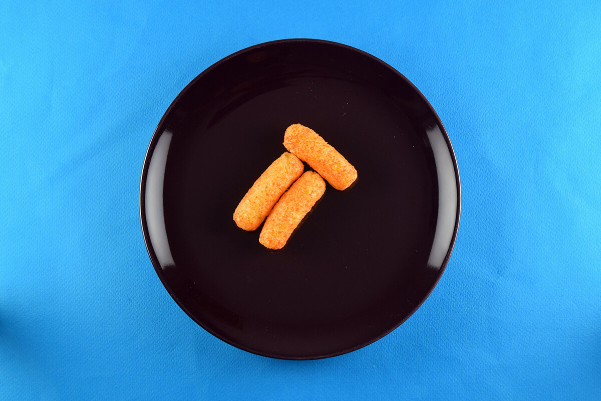 3 melty carrot puffs are placed onto a dark coloured plate to form the body of the rocket. 2 of them are placed vertically with 1 on top of them horizontally 
