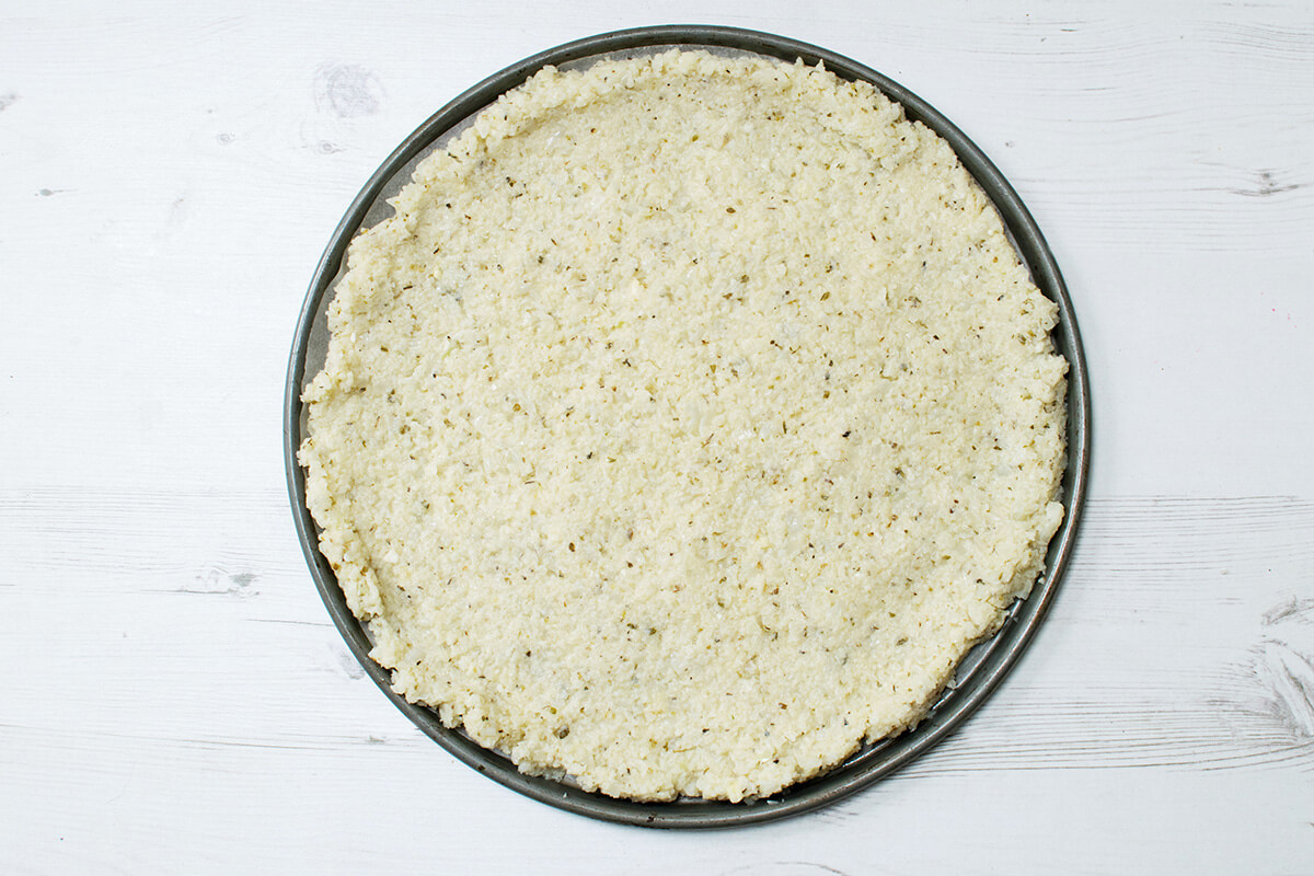 Cauliflower pizza base in a round baking tray
