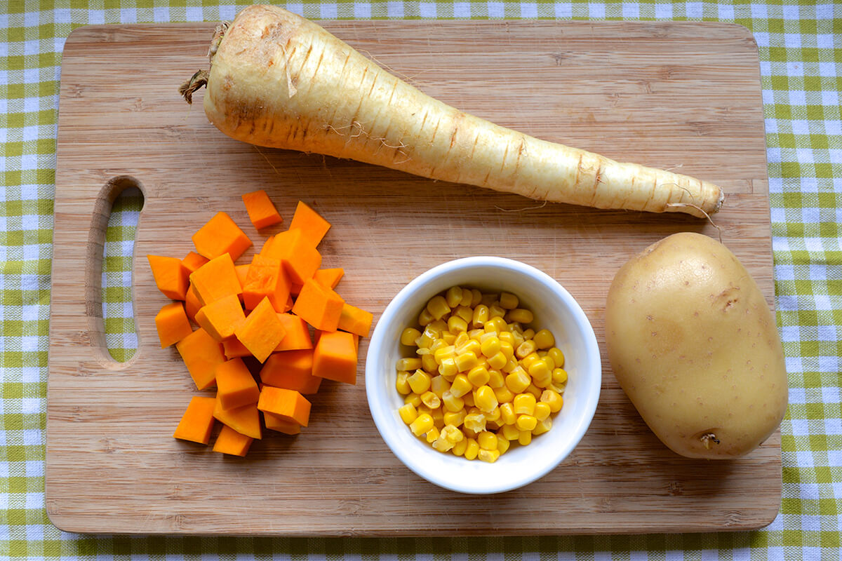 A chopping board with a parsnip, diced butternut squash, sweetcorn and a potato