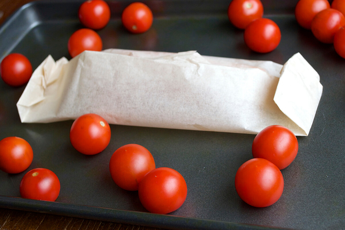 A baking tray with washed cherry tomatoes and a fillet of fish wrapped in the centre