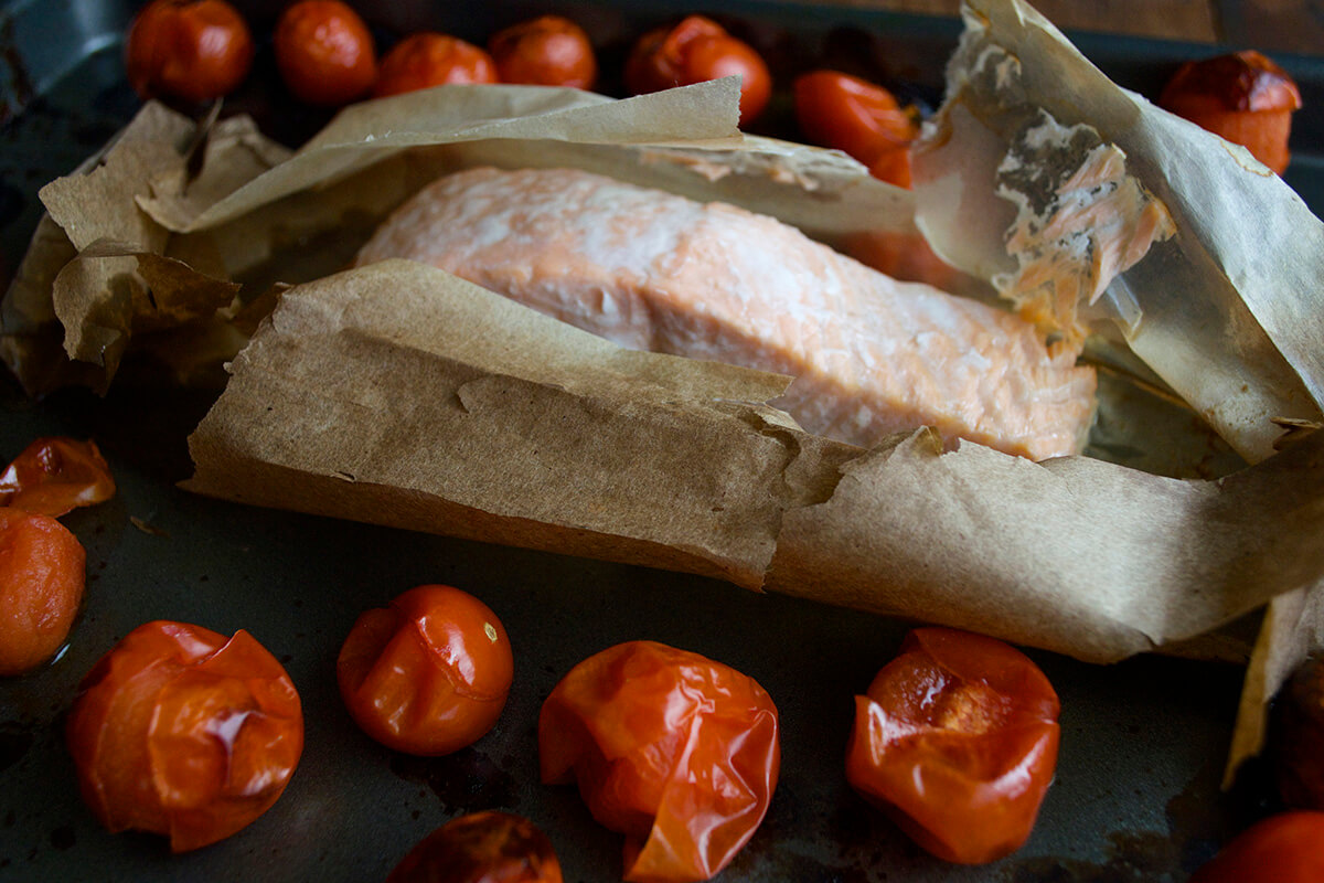 A baking tray with cooked cherry tomatoes and a fillet of cooked fish partially unwrapped in the centre