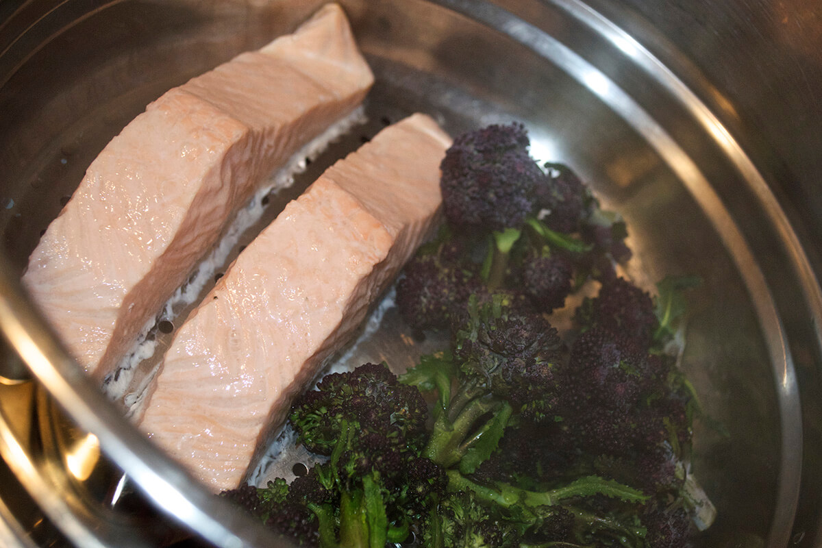 Two salmon fillets and purple sprouting broccoli in a steamer