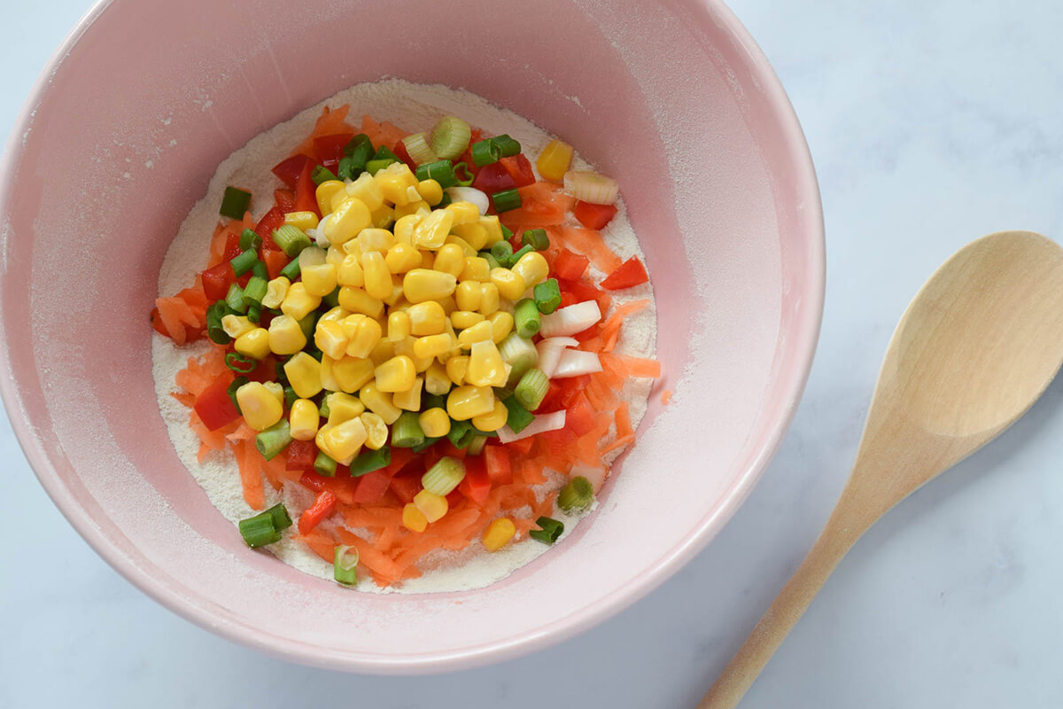 A bowl of flour with grated carrot, chopped spring onion, red pepper and sweetcorn