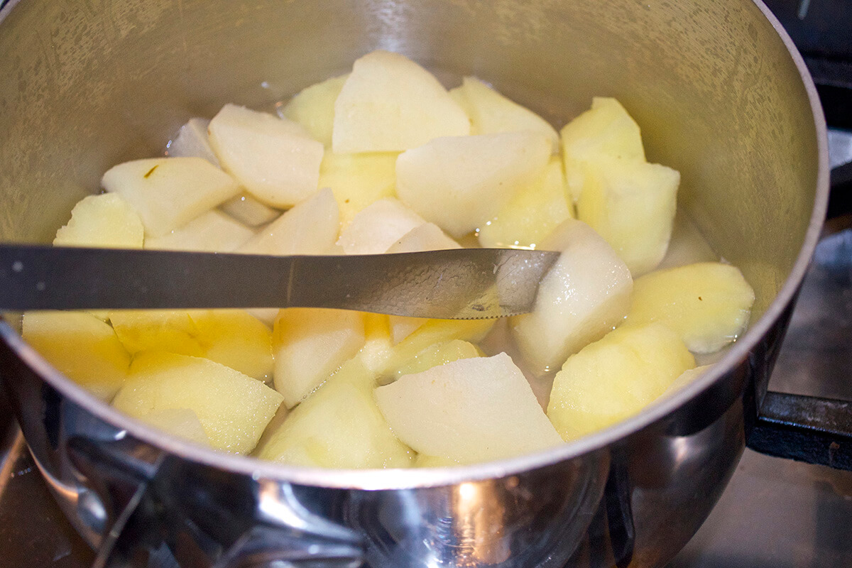 Diced apple in a saucepan of water being checked with a knife to see if it has softened