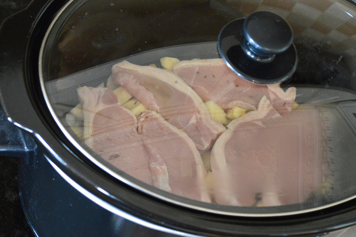 A slow cooker with cabbage, potato, onion, apple and pork