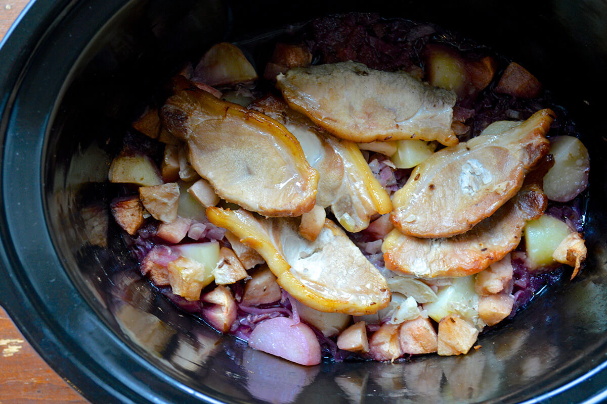 A slow cooker with cabbage, potato, onion, apple and pork with added seeds, and spice mixed with vinegar and stock