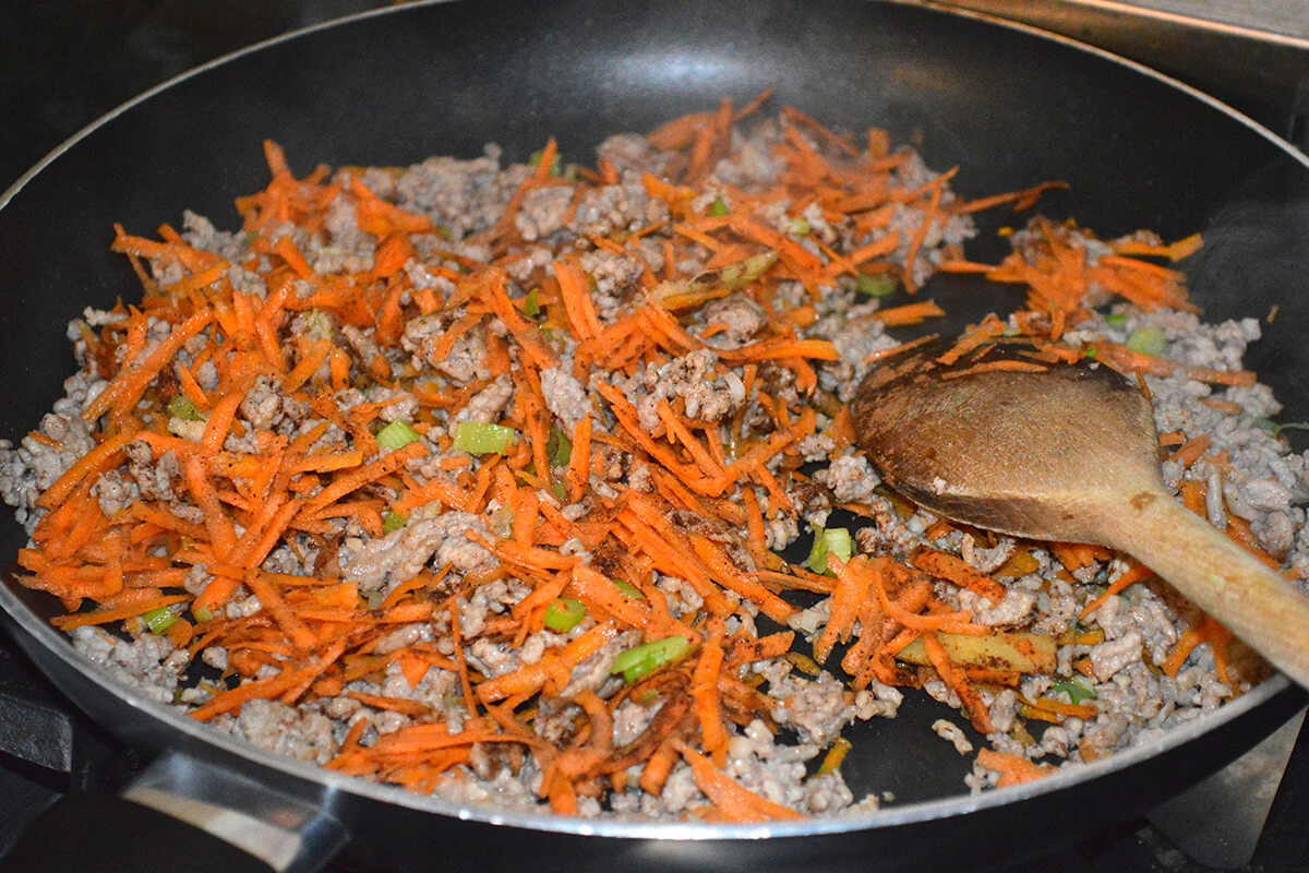 Minced pork and ginger in a frying pan with garlic, grated carrot, spring onion and Chinese 5 spice