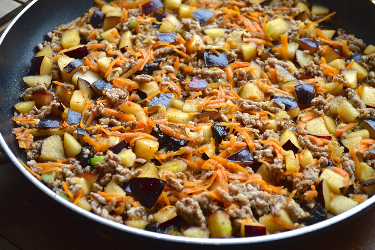 Minced pork and ginger in a frying pan with garlic, grated carrot, spring onion and Chinese 5 spice, plums and prunes