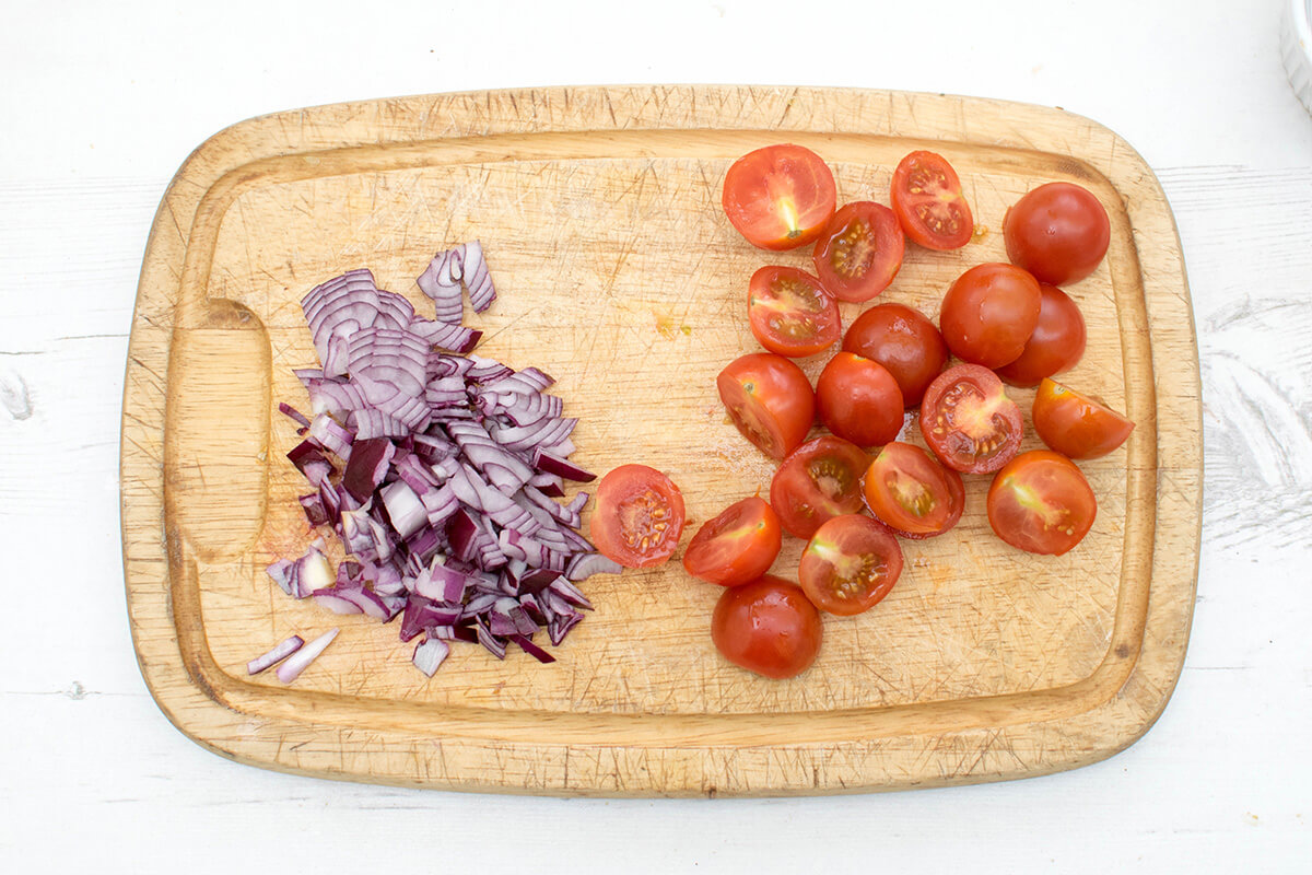 A chopping board with chopped red onion and halved cherry tomatoes