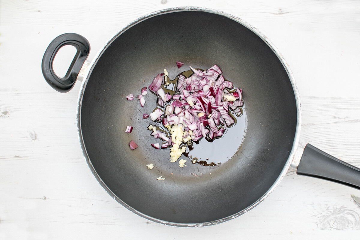 A wok with olive oil, chopped onion and crushed garlic