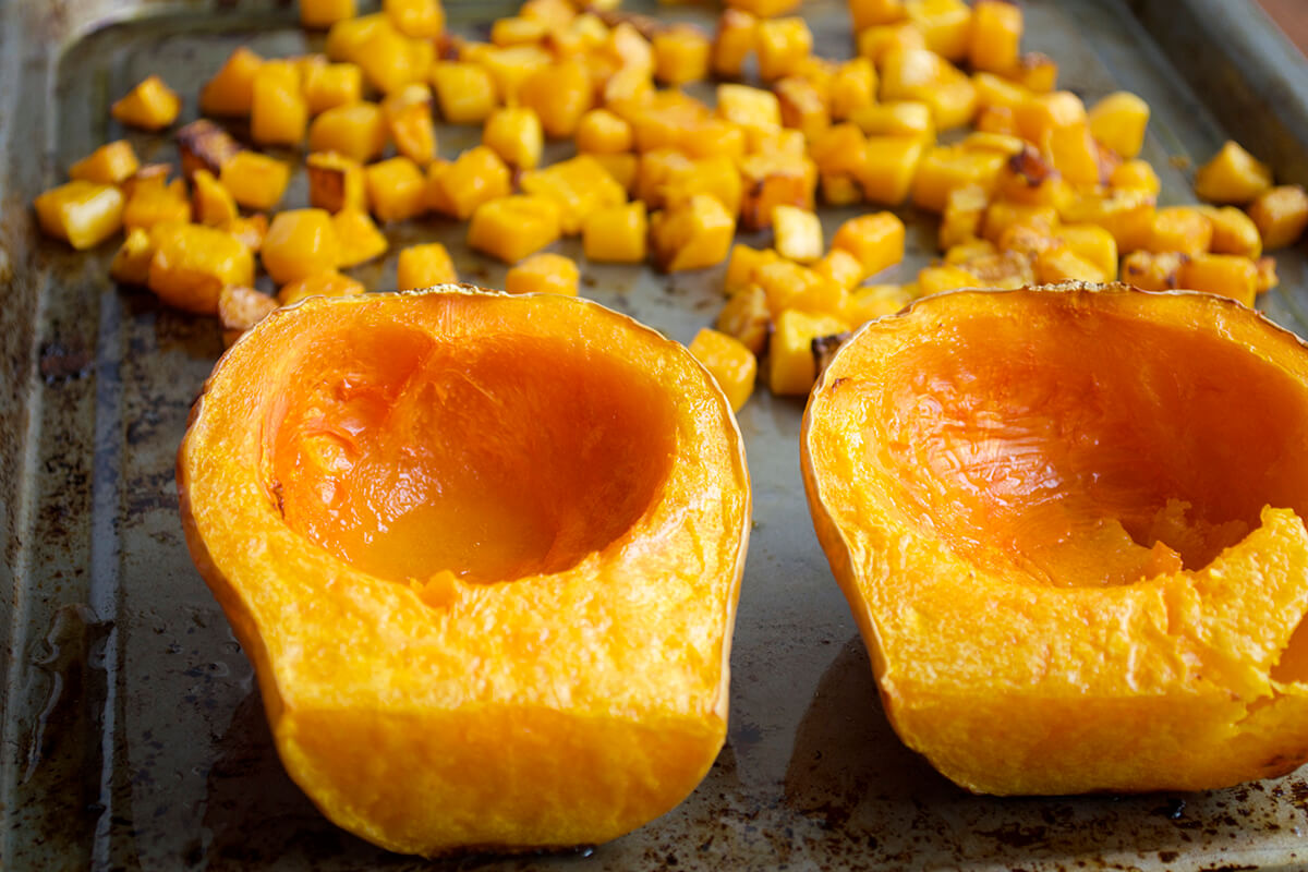 Halved, roasted butternut squash with some diced butternut squash next to it on a roasting tray