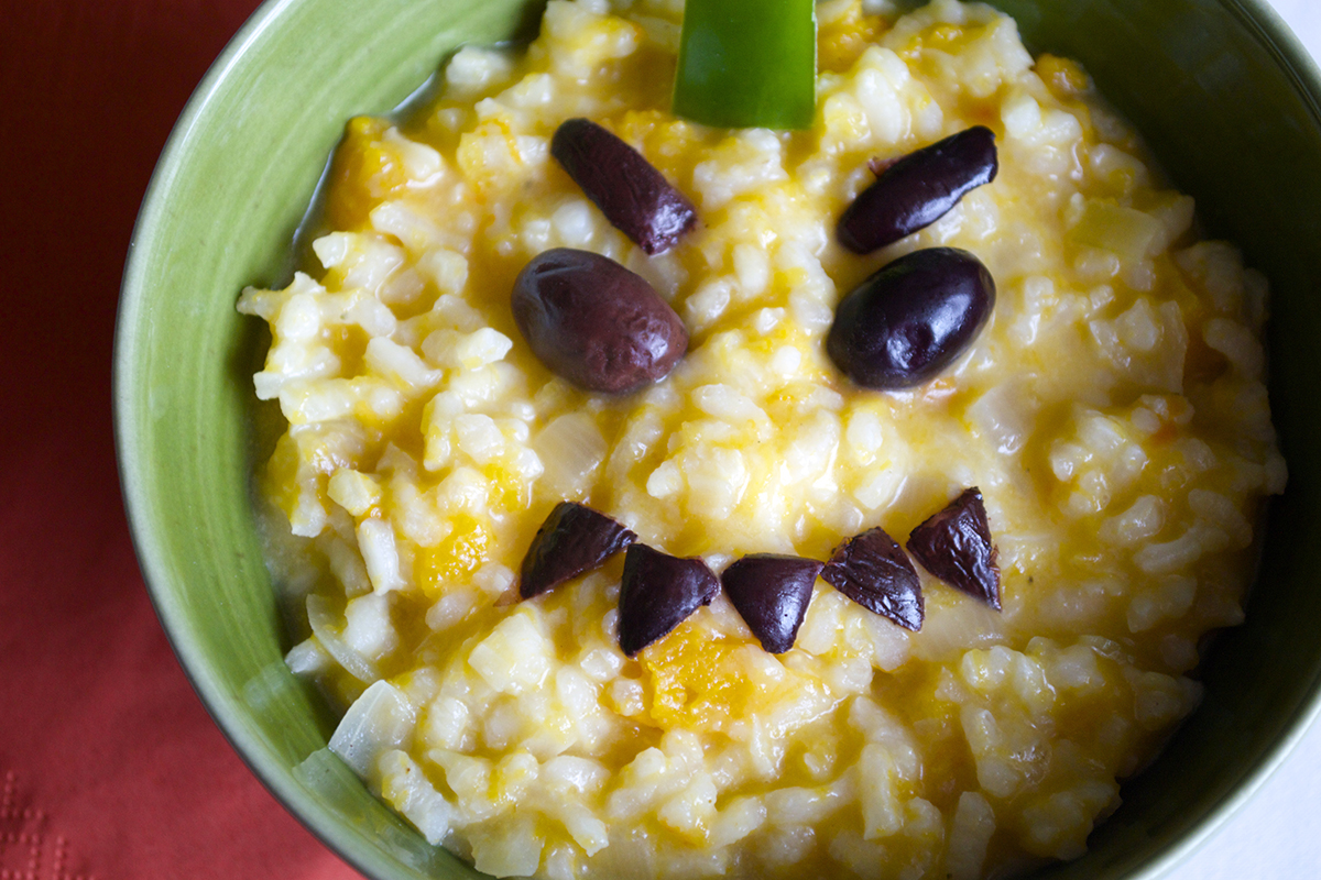 A bowl of butternut quash risotto with olives on top, creating a spooky pumpkin face