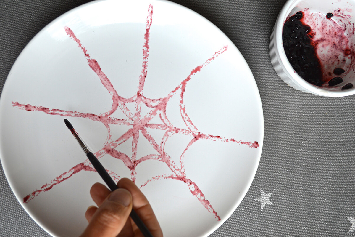The juice of crushed blackberries is painted onto a white plate in the shape of a spiders web