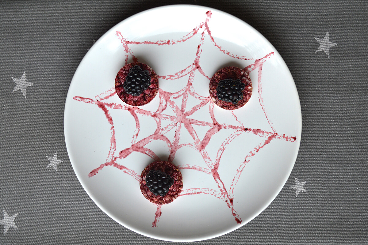 3 summer fruit rice cake clouds are placed onto the web and blackberry halves are placed on top of them to create the spiders bodies