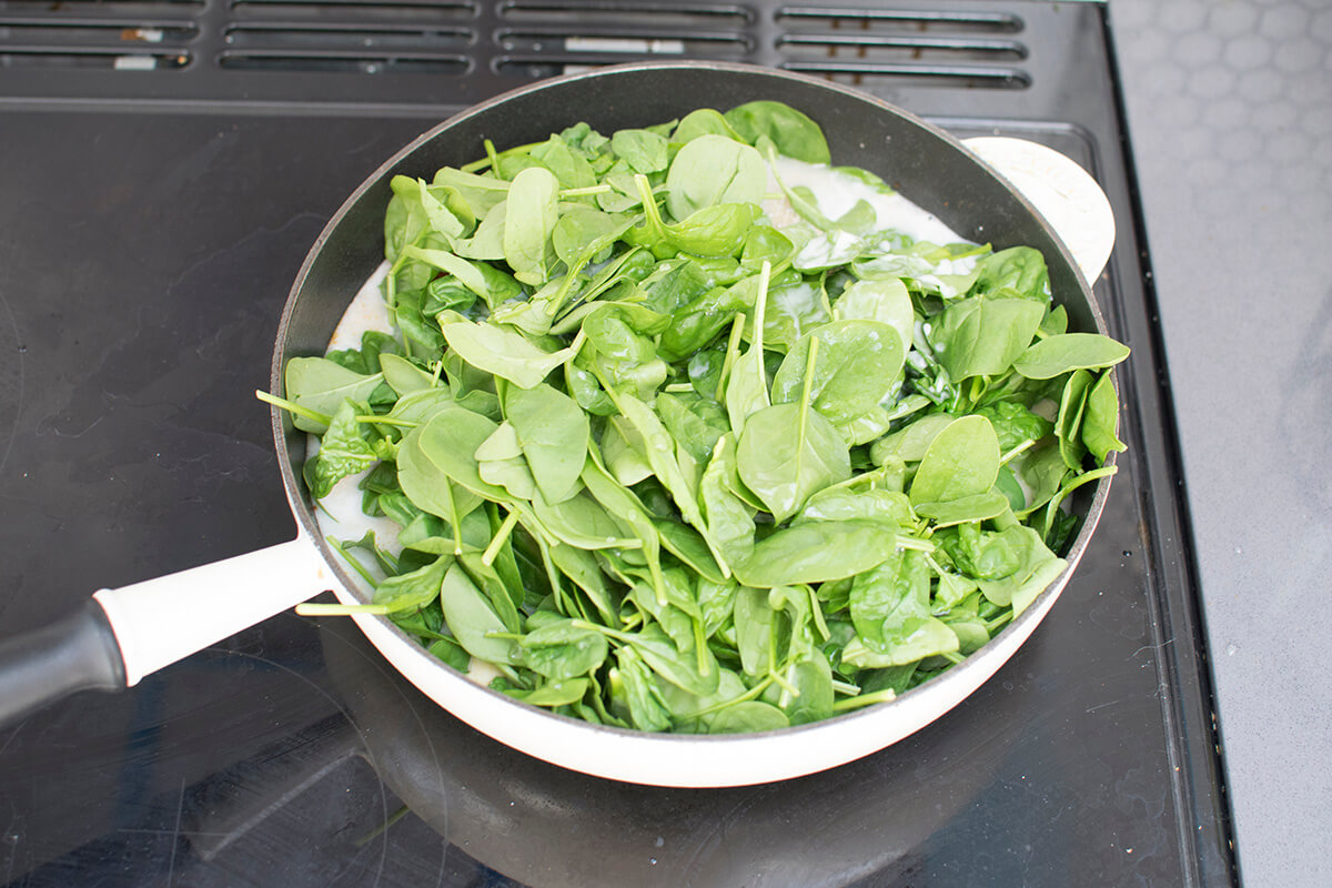 A saucepan with chopped tomatoes, coconut milk, stock and spinach