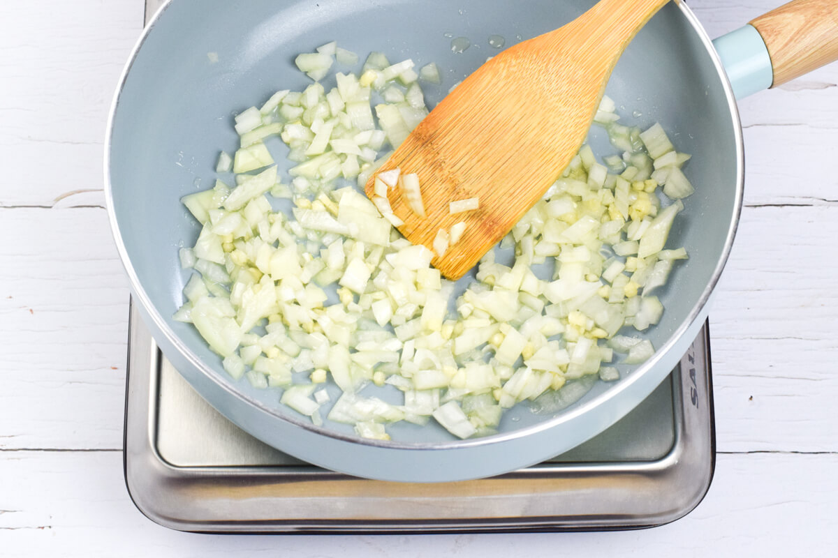 A frying pan with yellow onion and garlic being fried 