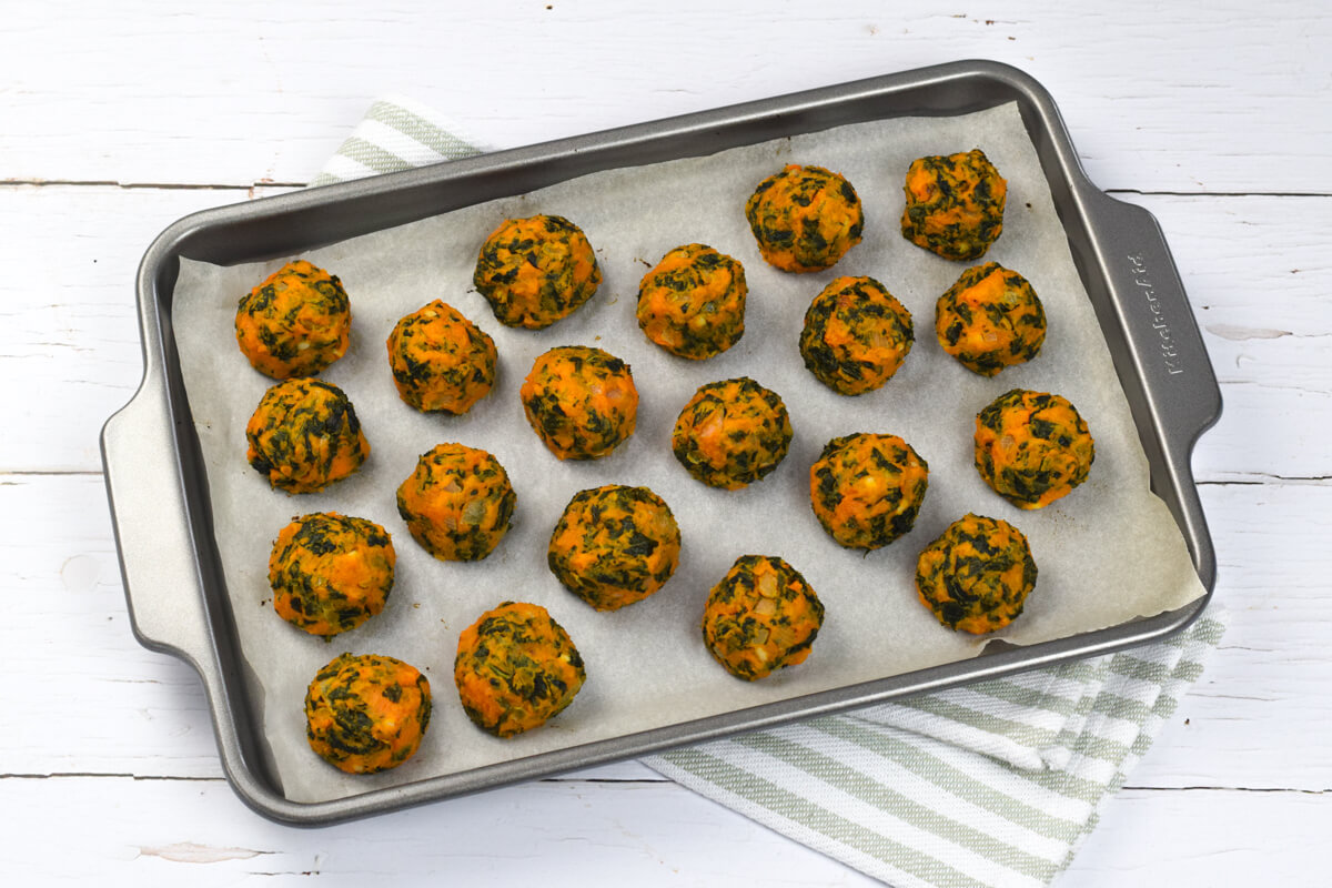 A lined baking tray with uncooked balls of sweet potato and kale bites