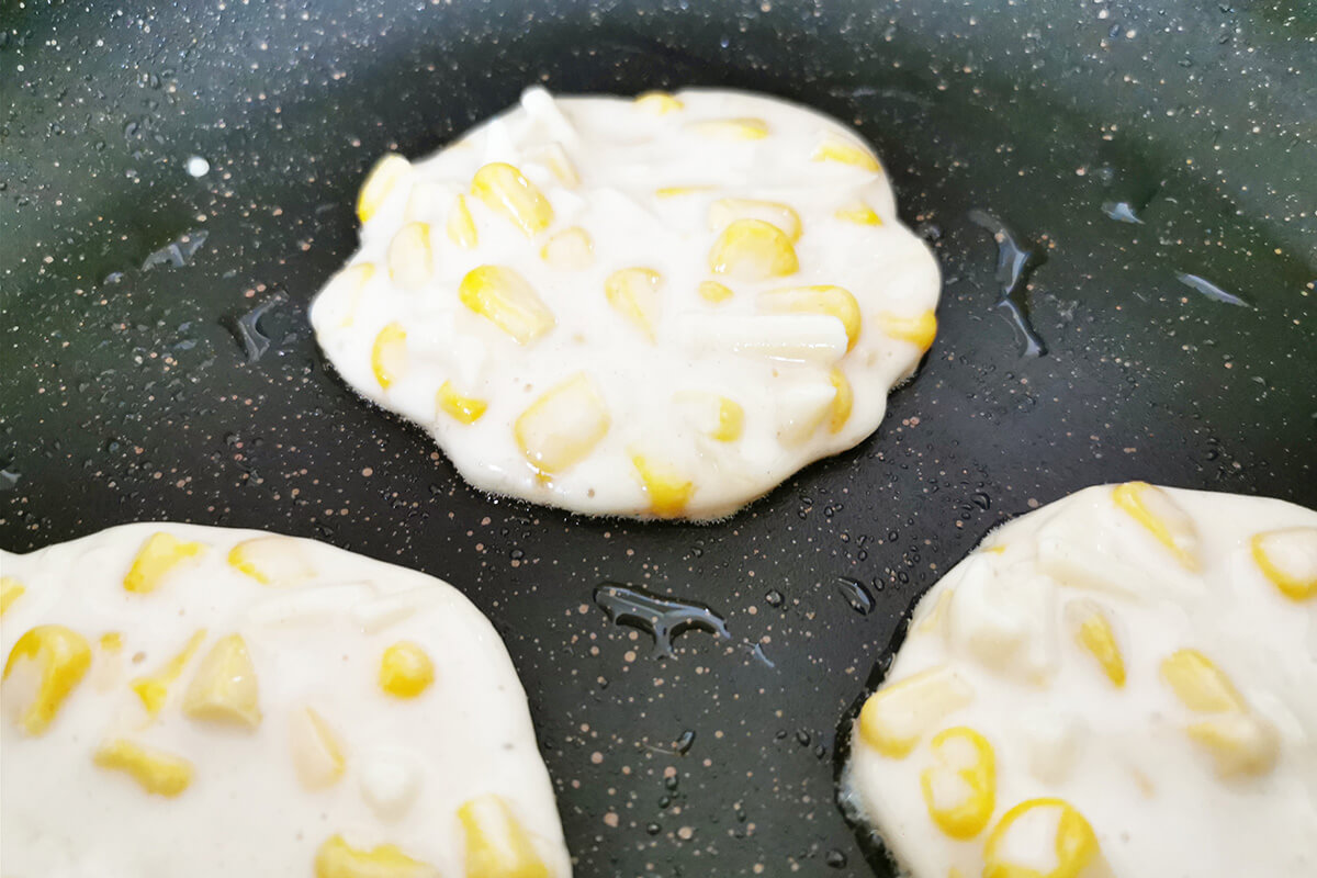 3 sweetcorn fritters being fried in a frying pan