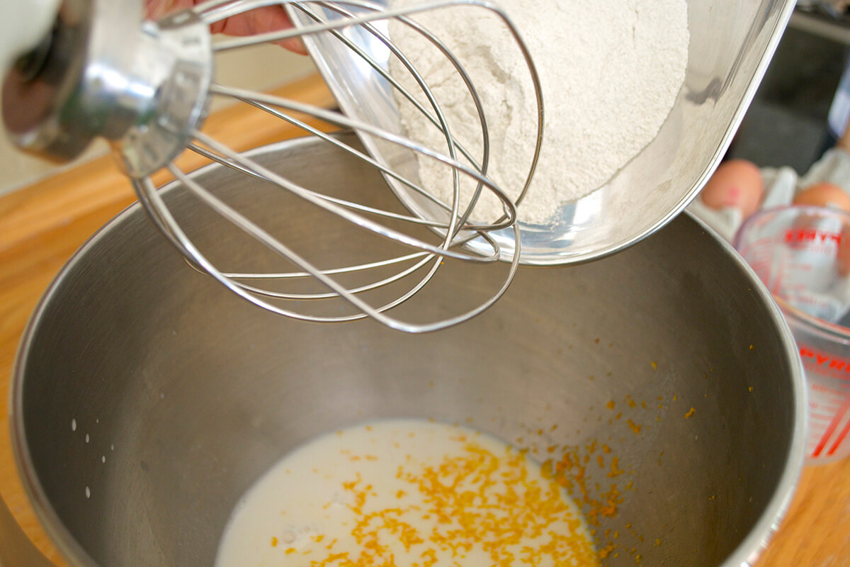 Flour being added to an orange zest pancake mix beneath an electric whisk