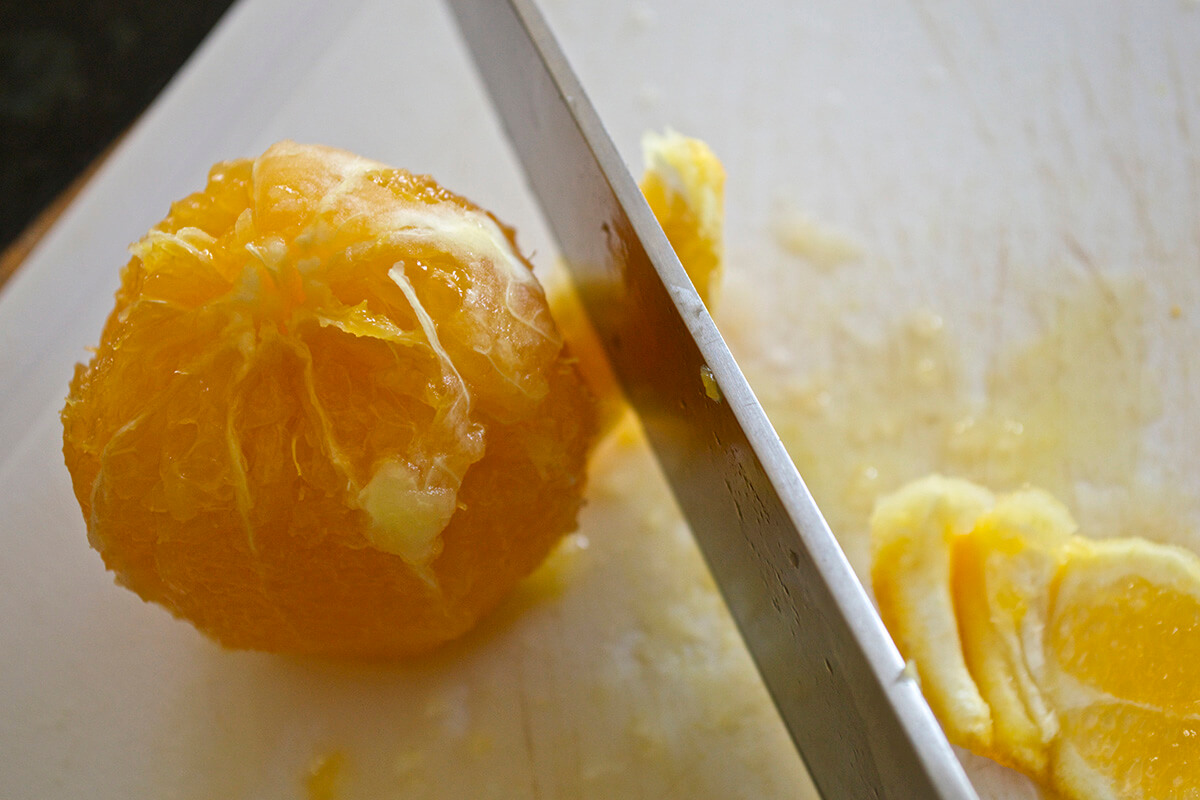 An orange on a chopping board having the pith removed