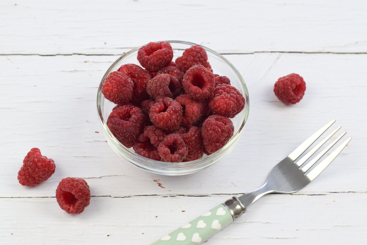 A bowl of whole raspberries next to a fork