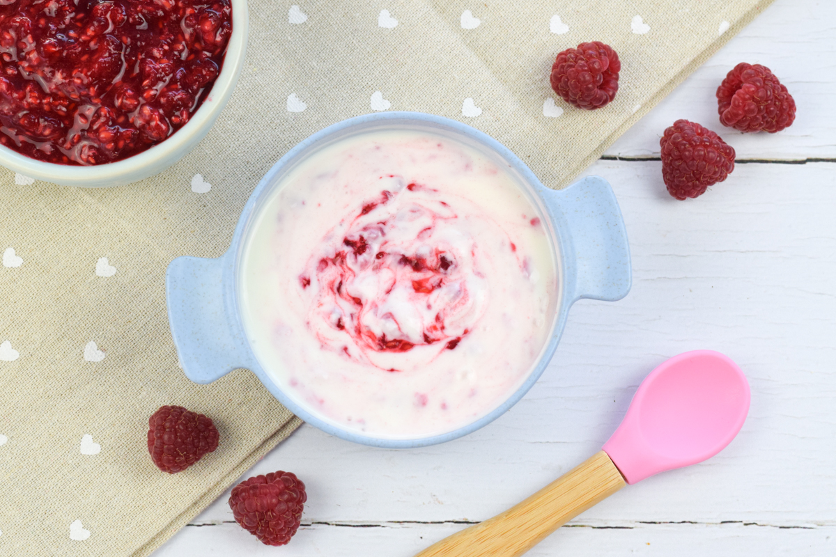 A bowl of yoghurt with mashed raspberries stirred into it, next to a bowl of whole raspberries